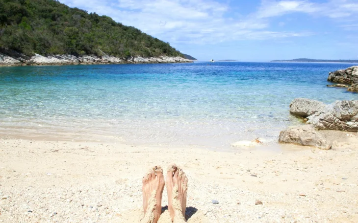 Pohled na bosé nohy v písku na slunné pláži s výhledem na moře, ideální zimní dovolená